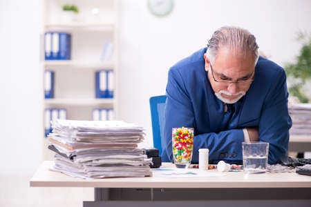 Old male sick employee working overtime in the officeの写真素材