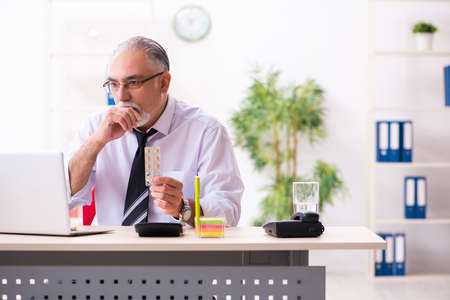 Old sick employee suffering at workplaceの写真素材