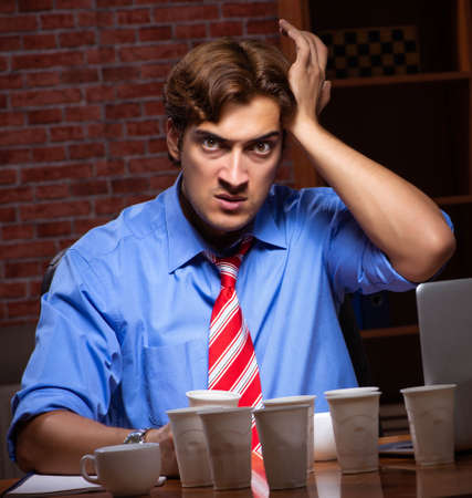 Young employee drinking coffee working at night shiftの写真素材