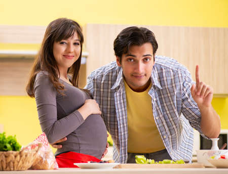 Man and pregnant woman preparing salad in kitchen