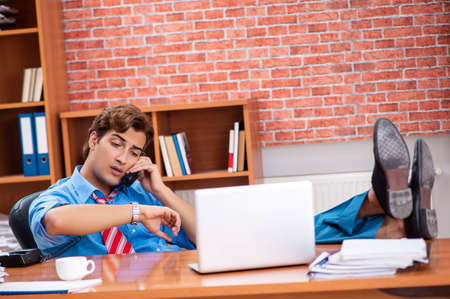 Young employee with excessive work sitting at the officeの写真素材