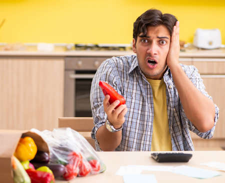 Young man calculating expences for vegetables in kitchenの写真素材
