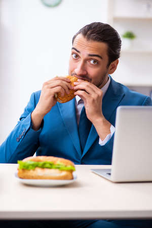 Young male employee having breakfast at workplaceの写真素材