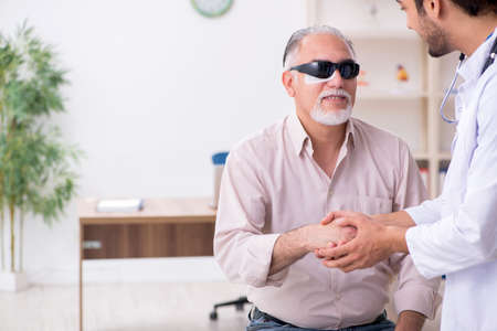 Old blind man visiting young male doctorの写真素材