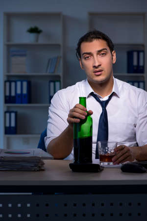Alcohol addicted businessman working late in the officeの写真素材