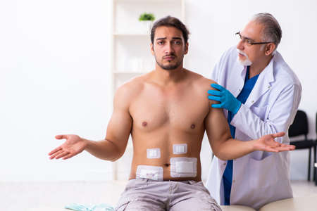 Injured young man visiting experienced male doctorの写真素材