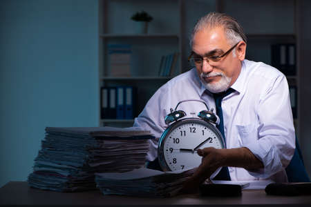 Old male employee working late in the officeの写真素材
