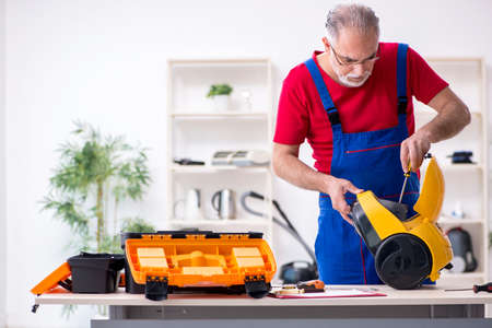 Old male contractor repairing vacuum cleaner indoorsの写真素材