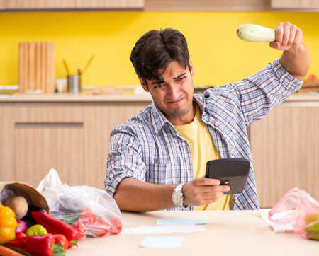 Young man calculating expences for vegetables in kitchenの写真素材