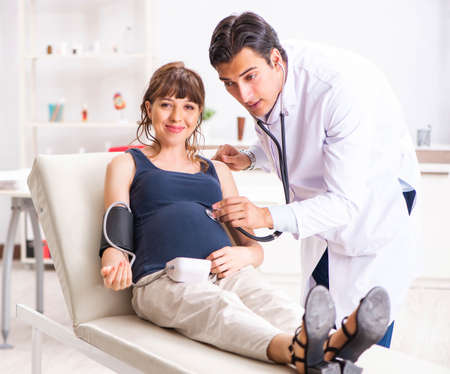 Young doctor checking pregnant womans blood pressure