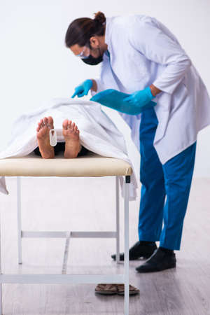 Police coroner examining dead body corpse in morgue