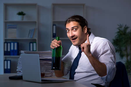 Alcohol addicted businessman working late in the officeの写真素材