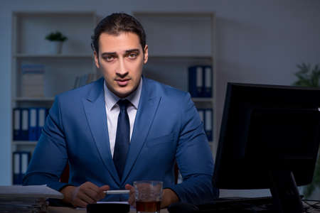 Alcohol addicted businessman working late in the officeの写真素材