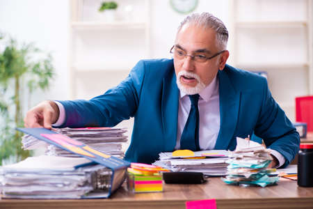 Old employee working in the office in conflicting prioritiesの写真素材