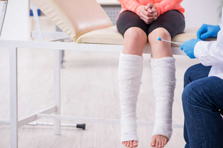 Young injured woman visiting old doctor traumatologistの写真素材