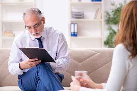 Young woman visiting old male doctor psychologistの写真素材