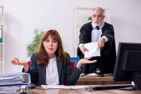 Old male judge and his young secretary in the officeの写真素材