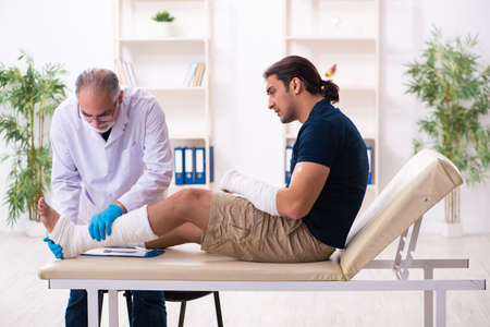Young injured man visiting old doctor traumatologistの写真素材