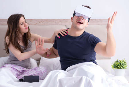 Wife and husband with virtual reality goggles in the bed