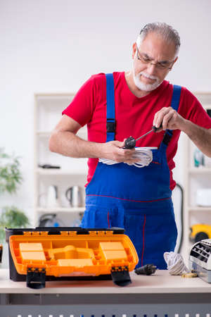 Old male contractor repairing air-conditioner indoorsの写真素材