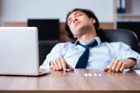 Young man having problems with narcotics at workplaceの写真素材