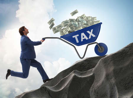 Businessman pushing tax wheelbarrow uphillの写真素材