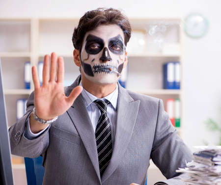 Businessmsn with scary face mask working in officeの写真素材