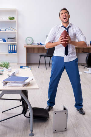 Young male employee throwing rugby ball in the office