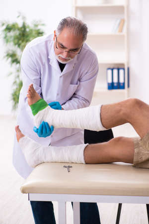 Young injured man visiting old doctor traumatologistの写真素材