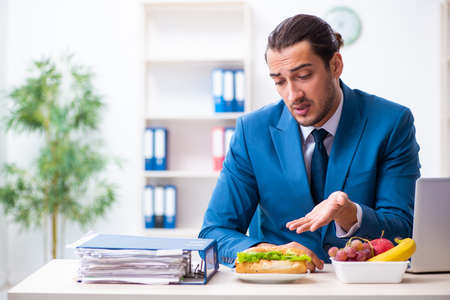 Young male employee having breakfast at workplaceの写真素材