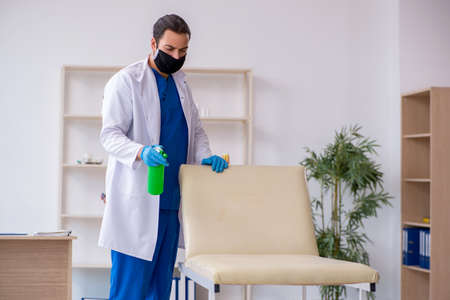 Young male contractor disinfecting clinic in pandemic conceptの写真素材