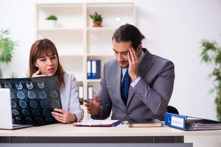 Young female doctor and sick businessman in the officeの写真素材