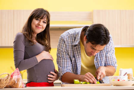 Man and pregnant woman preparing salad in kitchen