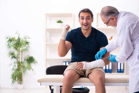 Young injured man visiting old doctor traumatologistの写真素材
