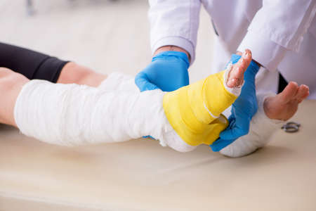 Young leg injured woman visiting old doctor traumatologistの写真素材