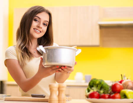 Young woman cooking soup in kitchen at homeの写真素材