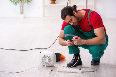 Young male contractor repairing fan heater indoorsの写真素材
