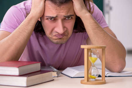 Young male student in the classroom at time management concept