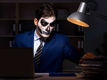 Businessman with scary face mask working late in officeの写真素材