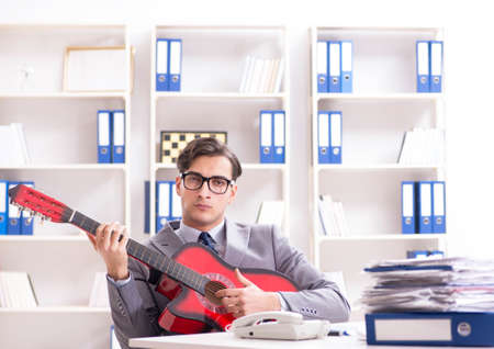 Young handsome businessman playing guitar in the officeの写真素材