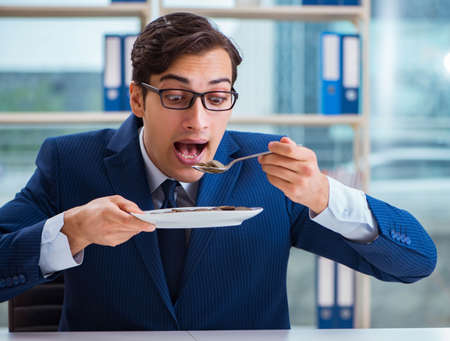 Funny businessman eating gold coins in officeの写真素材