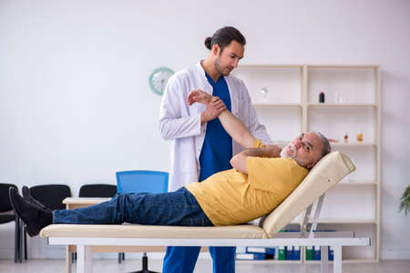 Old injured man visiting young male doctor chiropractorの写真素材