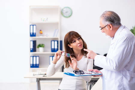 Young woman visiting old male doctor ophthalmologist