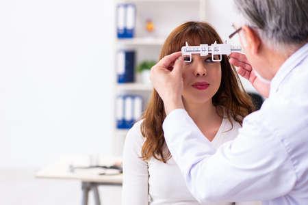 Young woman visiting old male doctor ophthalmologist