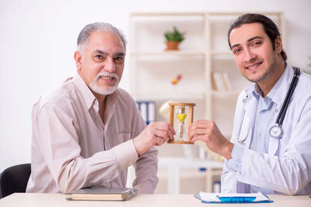 Old male patient visiting young doctor in time management concepの写真素材