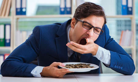 Funny businessman eating gold coins in officeの写真素材