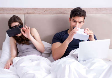 Wife and husband with virtual reality goggles in the bed
