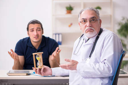 Young male patient visiting old doctor in time management concepの写真素材