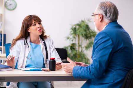 Old businessman visiting young female doctorの写真素材