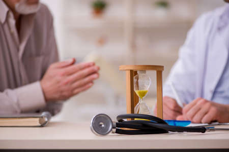 Old male patient visiting young doctor in time management concepの写真素材